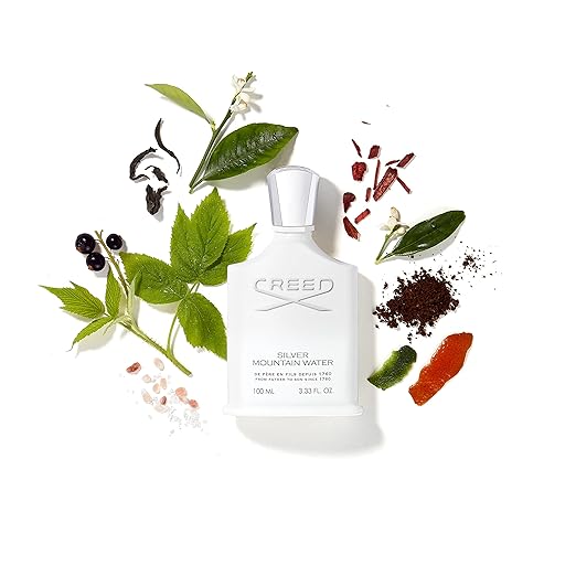 Creed Silver Mountain Water perfume bottle surrounded by leaves and flowers on a white background