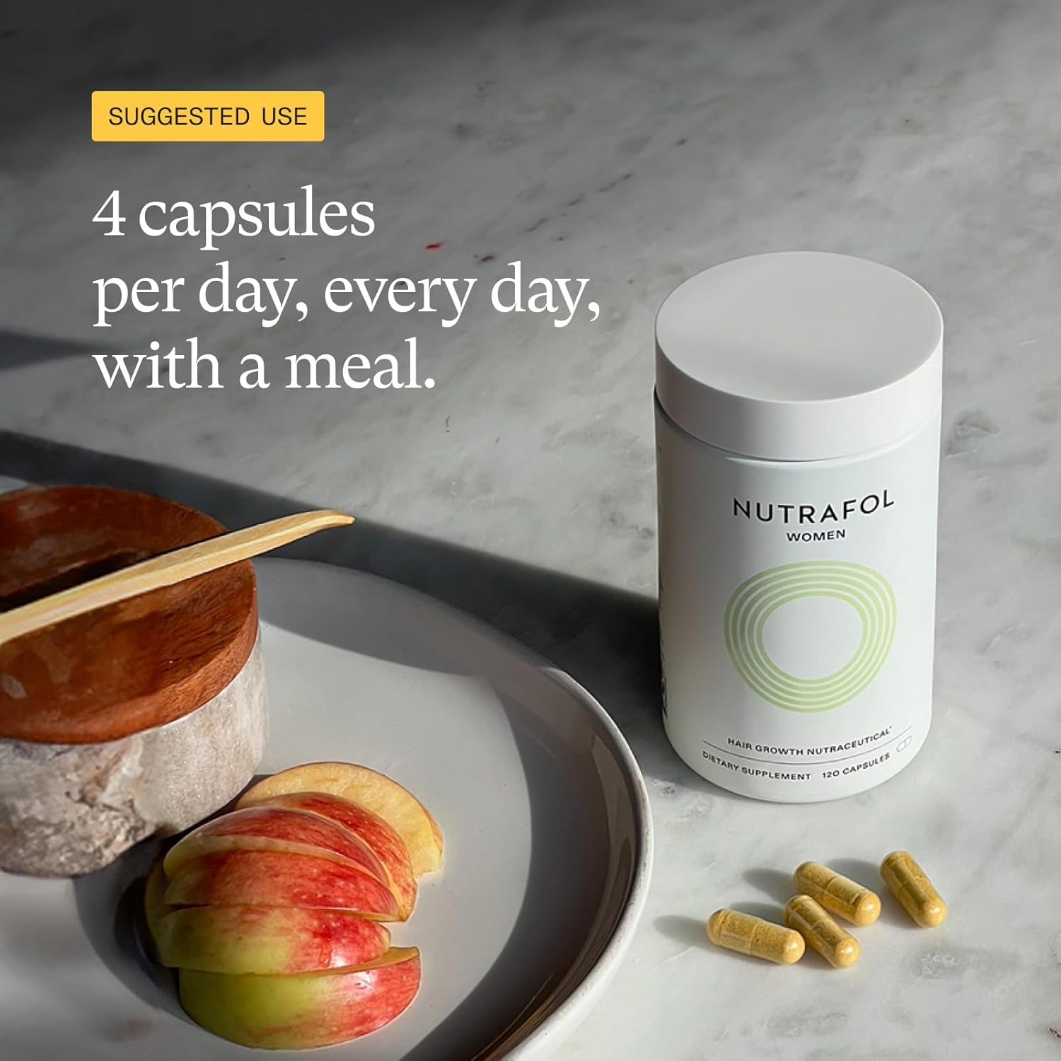 Nutrafol supplement container with capsules and apples on a marble surface