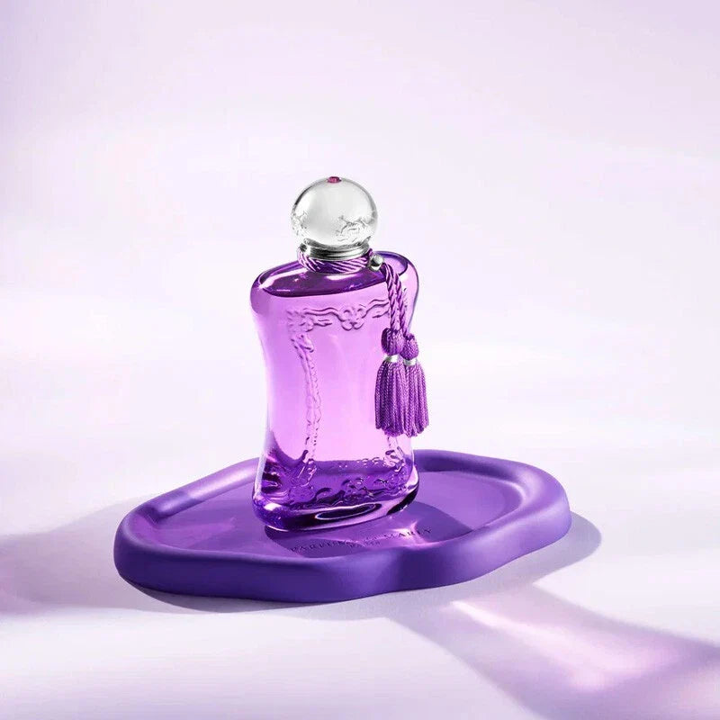 Purple perfume bottle with a tassel on a matching purple stand against a light purple background