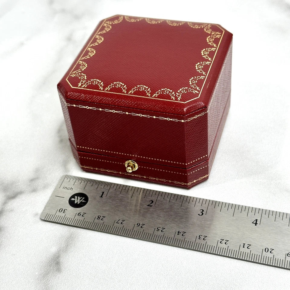 Red jewelry box with gold accents next to a ruler on a marble surface