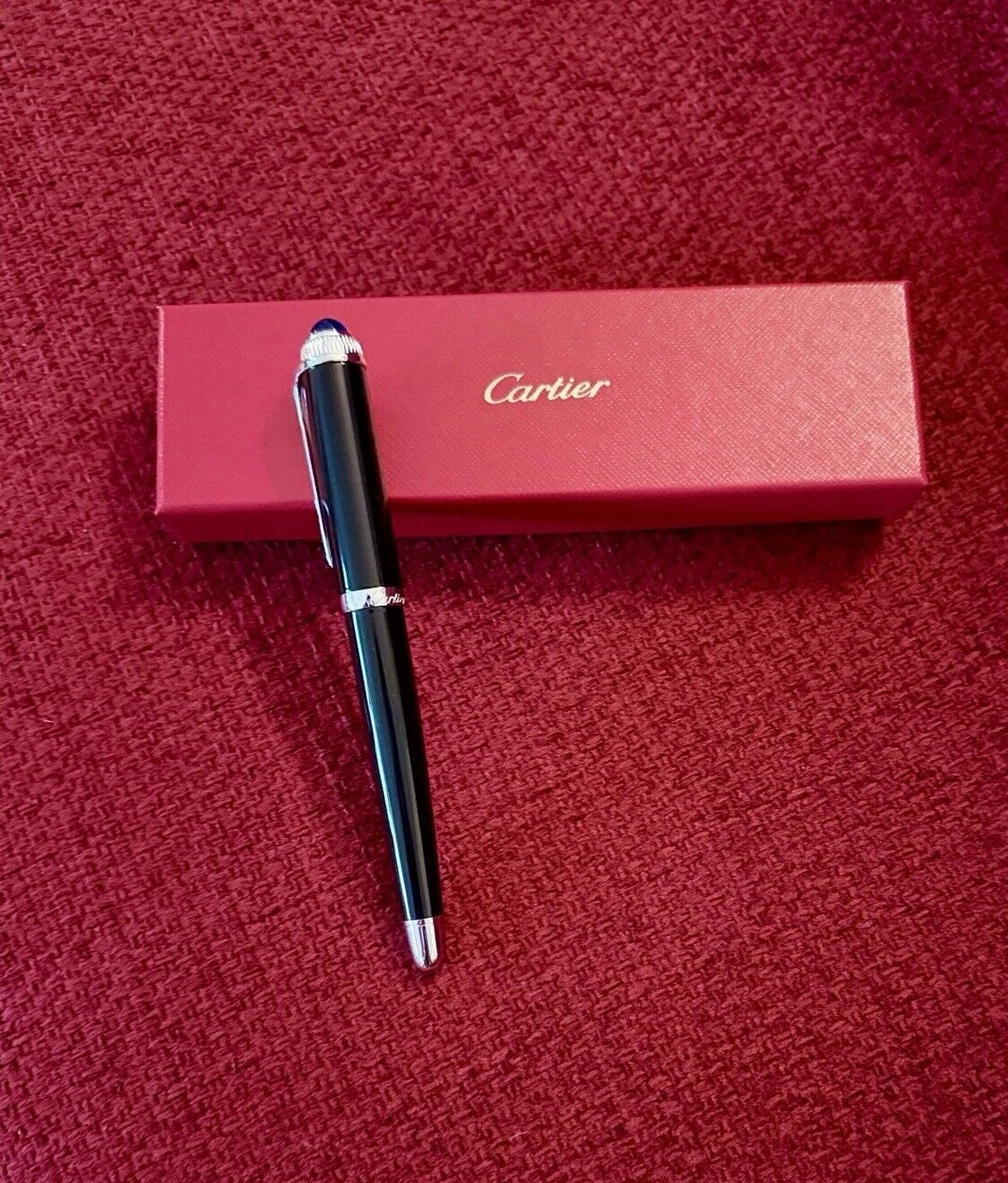 Cartier pen on a red textured surface with Cartier box in the background