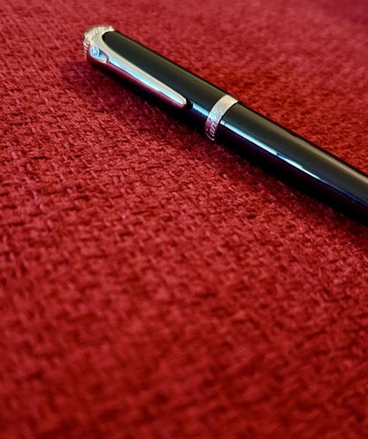 Black pen with silver cap on a red textured surface