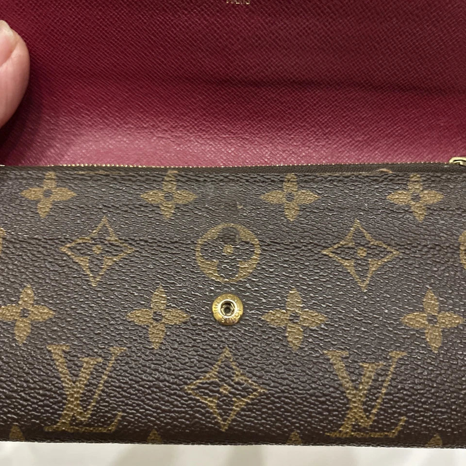 Close-up of a brown leather wallet with gold monogram pattern, held by a hand against a red background.