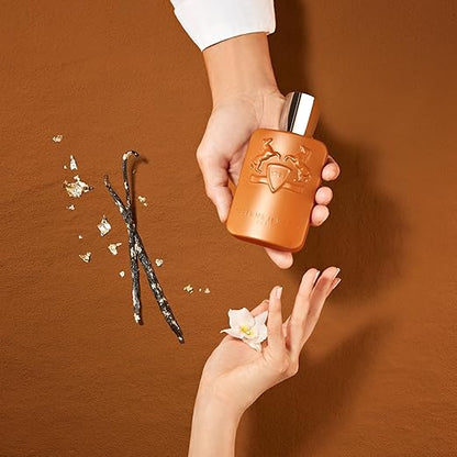 Hand holding a brown perfume bottle with vanilla beans and a flower on a brown background
