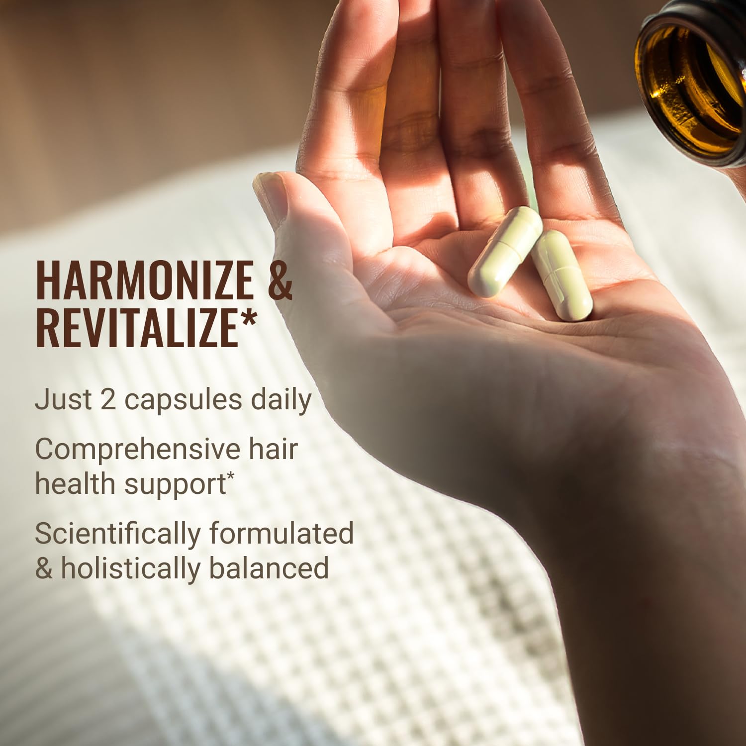 Hand holding two capsules with promotional text about hair health support on a blurred background