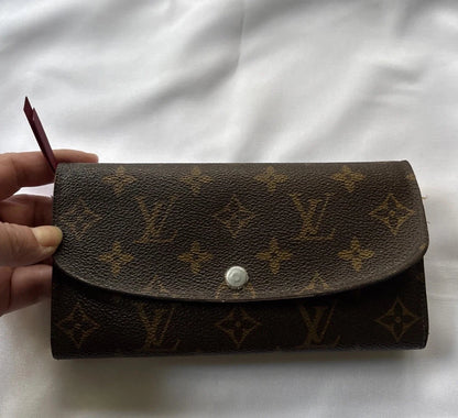 Louis Vuitton wallet with monogram pattern held by a hand on a white background