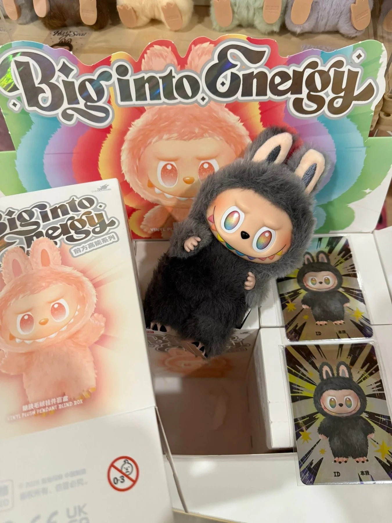 Plush toy and packaging with 'Big into Energy' branding on a colorful background.