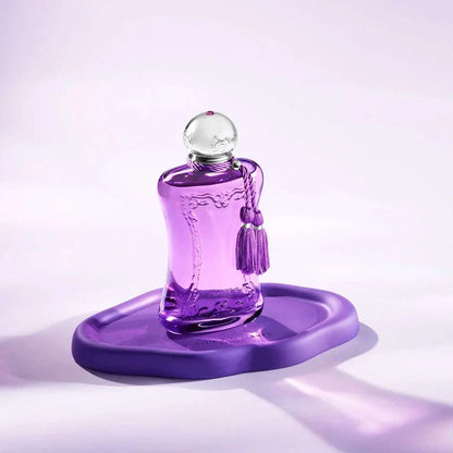 Purple perfume bottle with a tassel on a matching purple stand against a light purple background