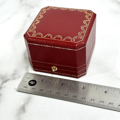 Red jewelry box with gold accents next to a ruler on a marble surface