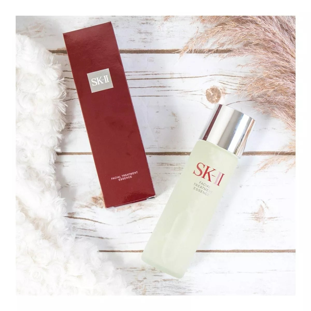SK-II facial treatment essence bottle and box on a wooden surface with decorative elements.