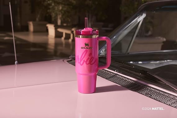 Pink tumbler with handle on a car hood, featuring a logo and text.