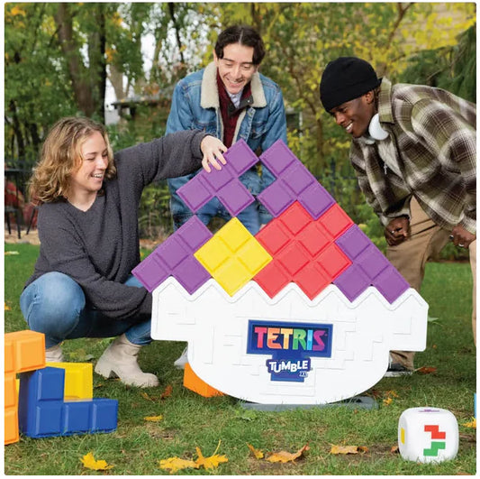 Three people playing with a large Tetris-themed tumbling toy outdoors.